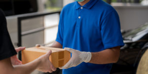 Corona Virus concept, Blue Delivery handsome asian man holding parcel cardboard box and thumbs up with protection mask and medical rubber gloves standing in front of the van