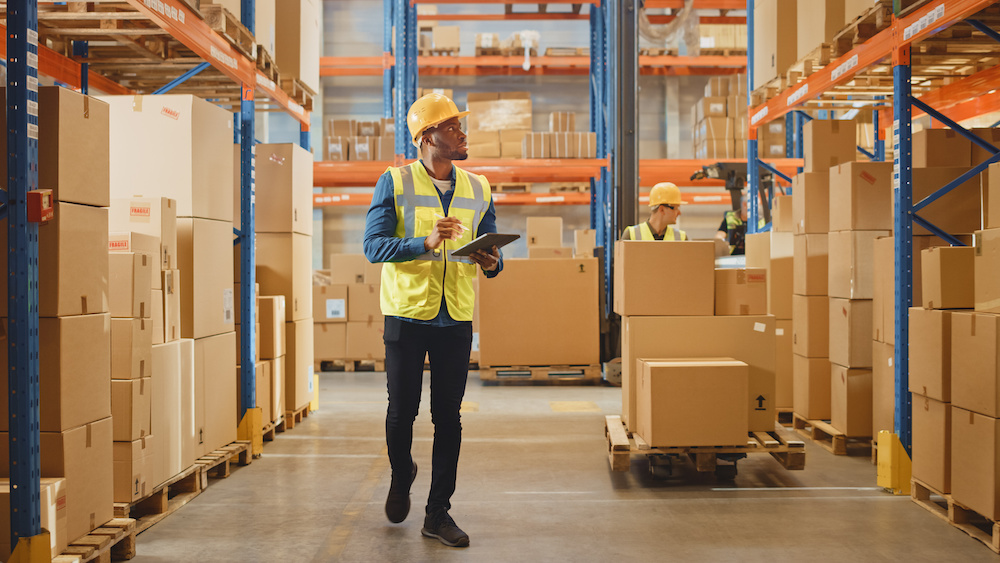 Male worker wearing hardhat in warehouse with tablet