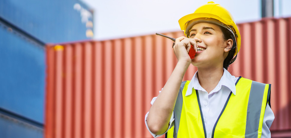 woman in hard hat on radio in front of cargo