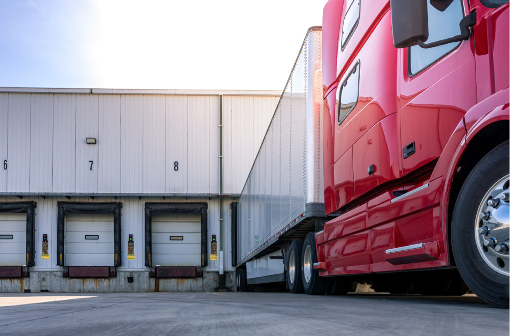 A red, modern semi-truck trailer parked at a loading dock to receive a shipment